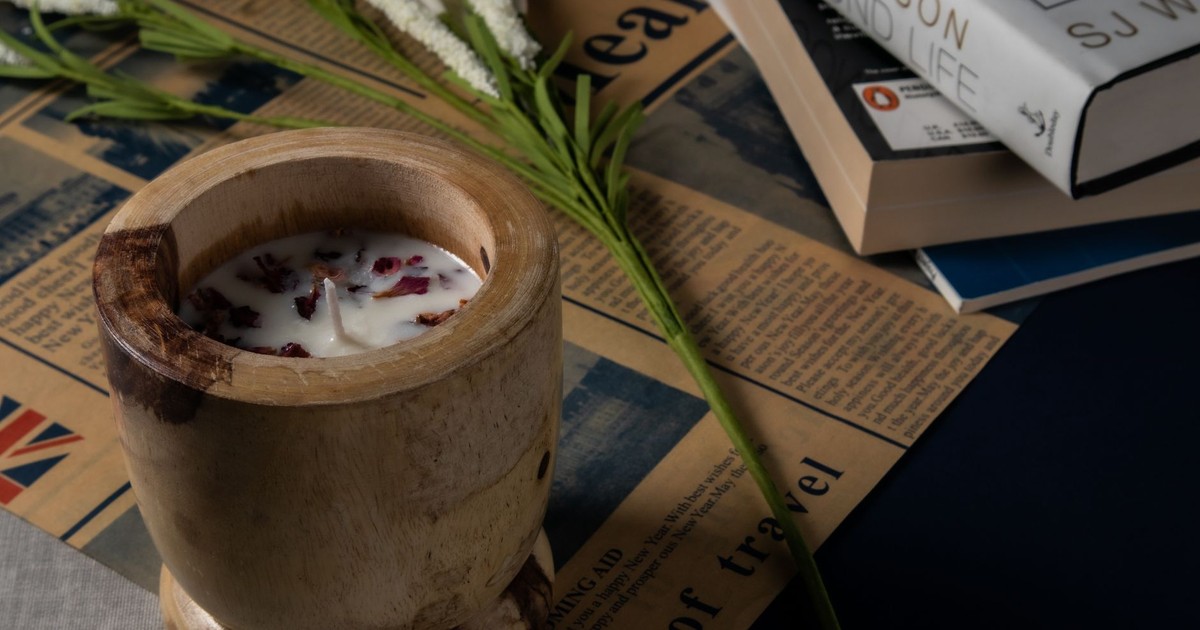 Cozy scene with a rustic wooden candle holder, books, and delicate flowers on a vintage newspaper background.