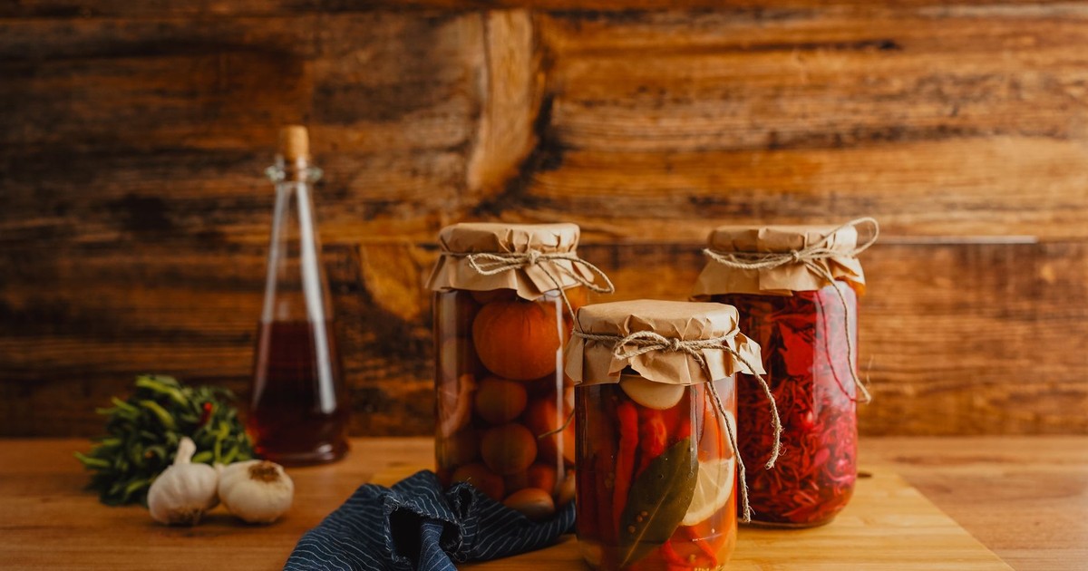Jars of preserved vegetables on a wooden surface with a rustic background.