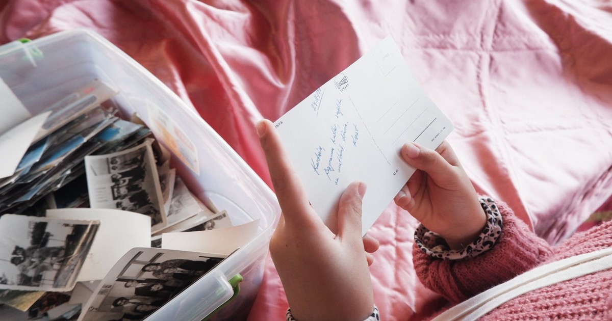 Close-up of a woman holding a postcard, exploring memories from a photo box.