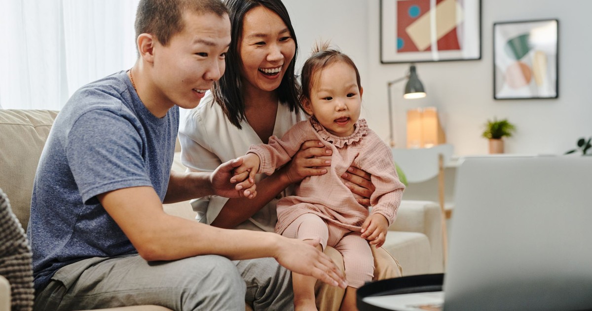 Smiling Asian family sitting on couch having a video call. Perfect for technology and lifestyle themes.