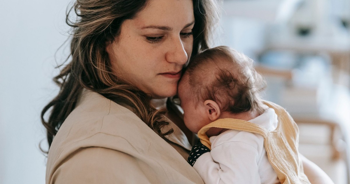 A mother gently holding her baby in a comforting embrace inside a cozy home setting.
