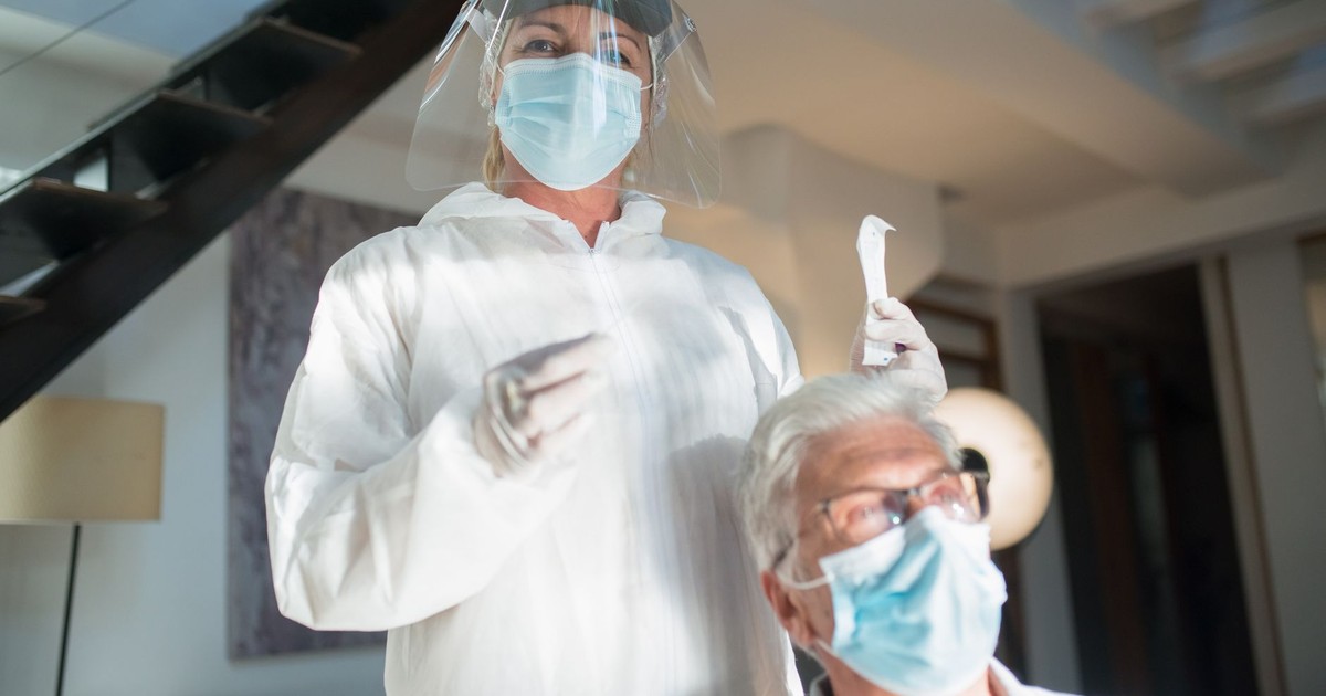 Healthcare professional in protective gear assisting elderly patient in a modern setting.