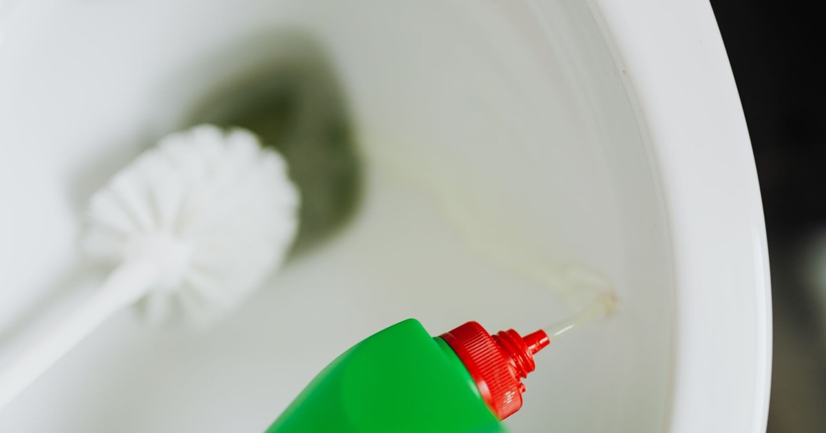 Top view of liquid detergent pouring from green plastic bottle in toilet bowl with toilet brush