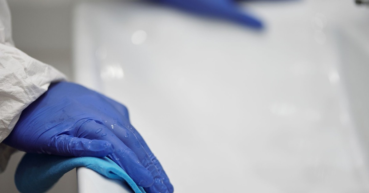 Close-up of a person sanitizing a bathroom sink with gloves and cloth, focusing on hygiene and cleanliness.