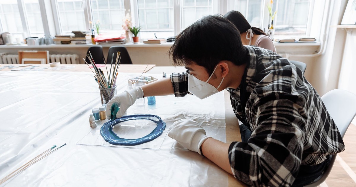 Asian man wearing face mask creating resin art at a bright indoor workspace.