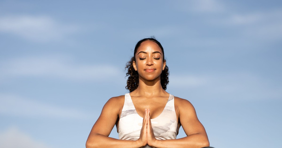 A woman meditating outdoors with eyes closed under a blue sky, embracing peace and mindfulness.