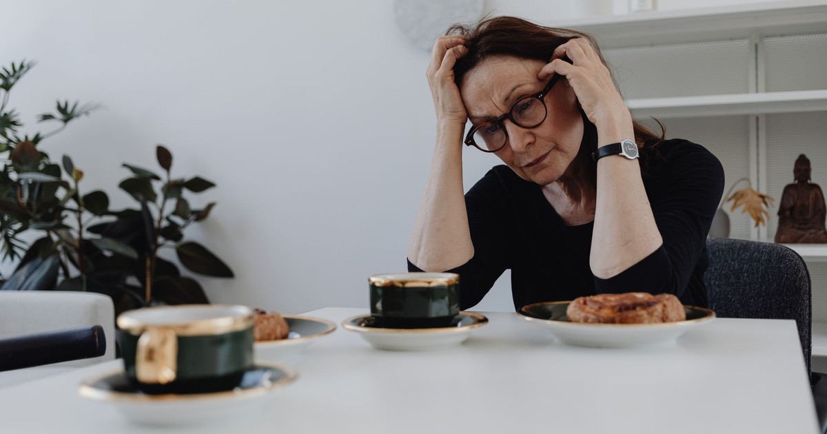 A woman sits alone at a table, expressing sadness and grief in a quiet home setting.