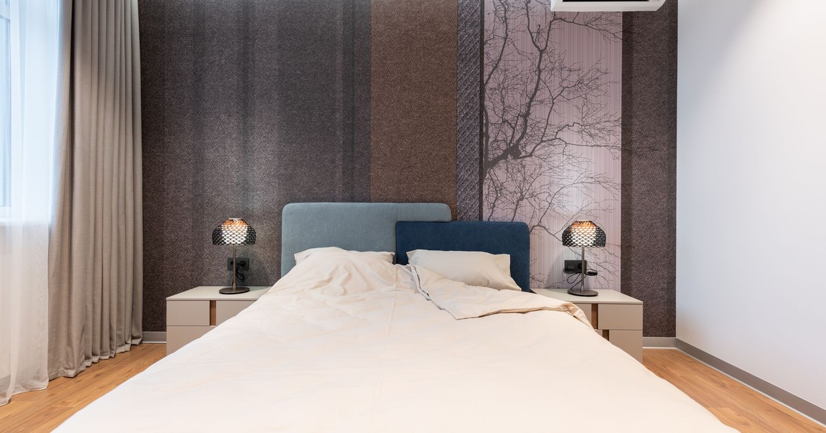 Interior of modern bright room with bed near table with lamp near wall and window with curtains and wooden floor