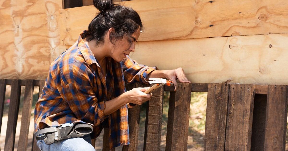 A woman hammering nails into wooden boards, engaged in a woodwork project in an outdoor setting.