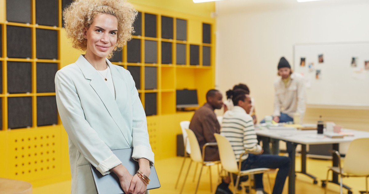 Confident businesswoman standing while a creative team collaborates in a modern office setting.