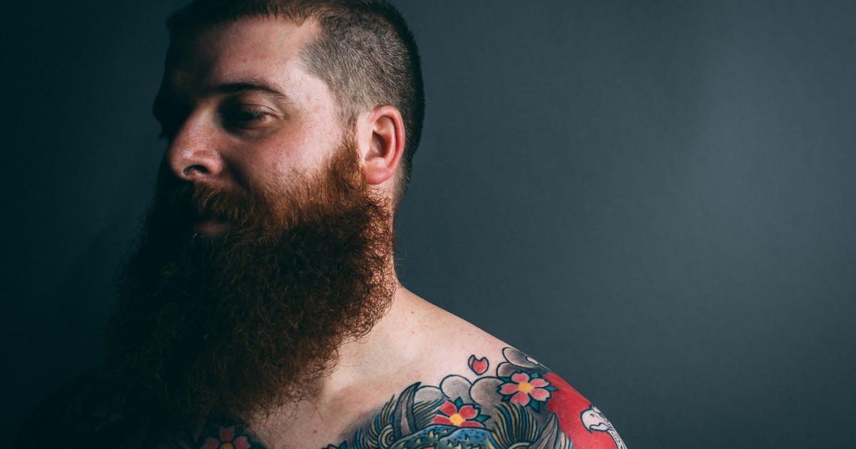 Portrait of a tattooed man with a beard in dramatic lighting.