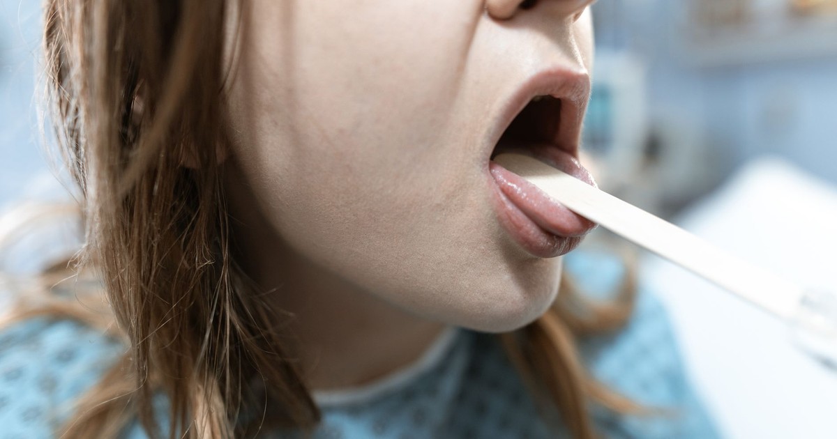 Close-up of a woman having her throat examined in a medical setting with a tongue depressor.