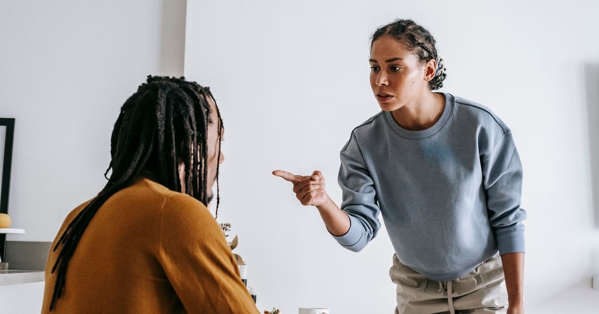Young African American female standing near table while male sitting at kitchen and having argument