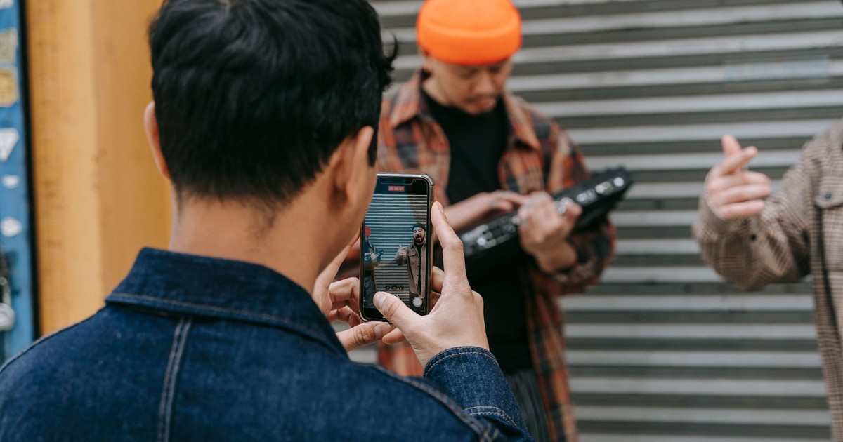 A person takes a photo of street musicians using a smartphone in an urban setting.