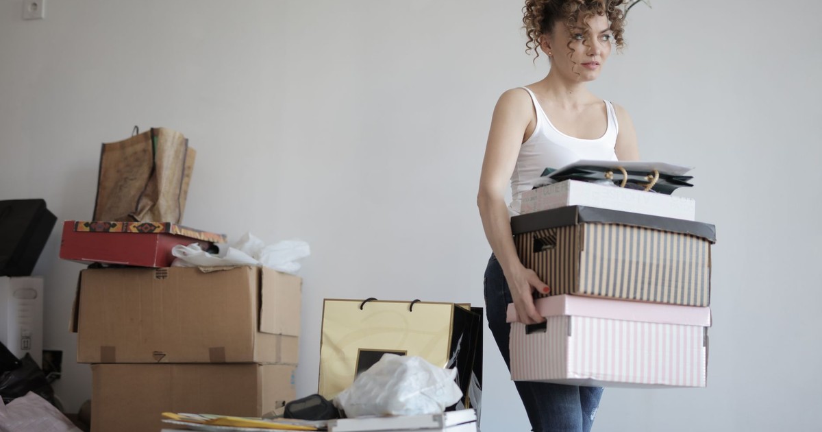 Focused female in casual clothing packaging belongings in boxes for moving in new apartment while standing in messy room and looking away