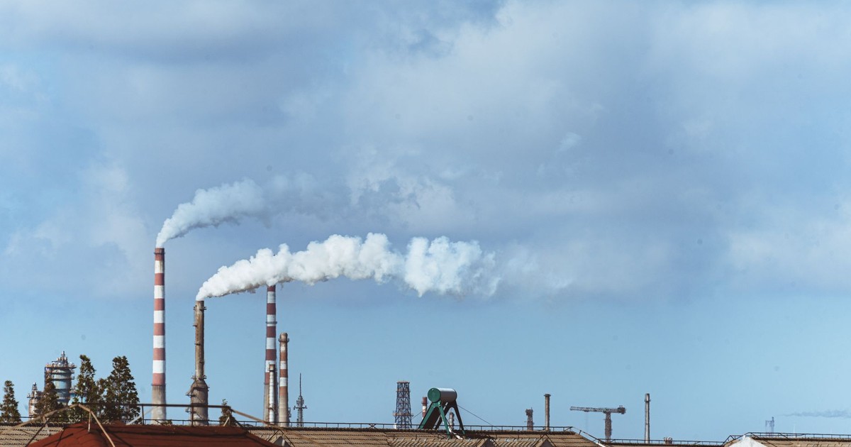 Factory chimneys emitting smoke over rooftops on a clear day, illustrating urban pollution.