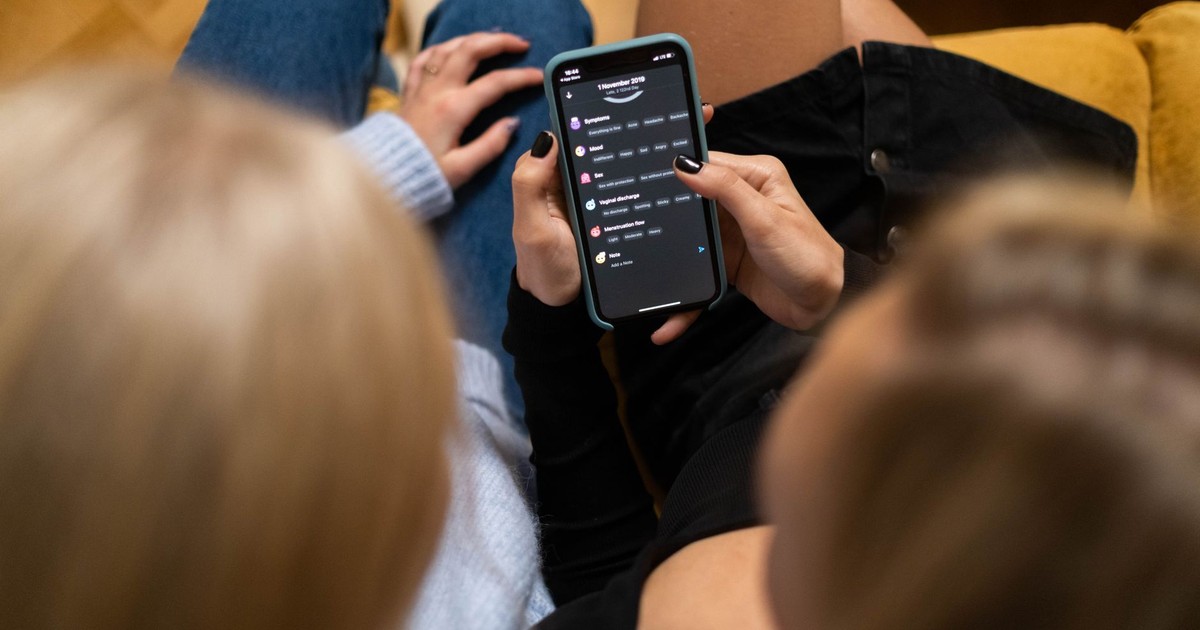 Two women browsing social media together on a smartphone indoors.