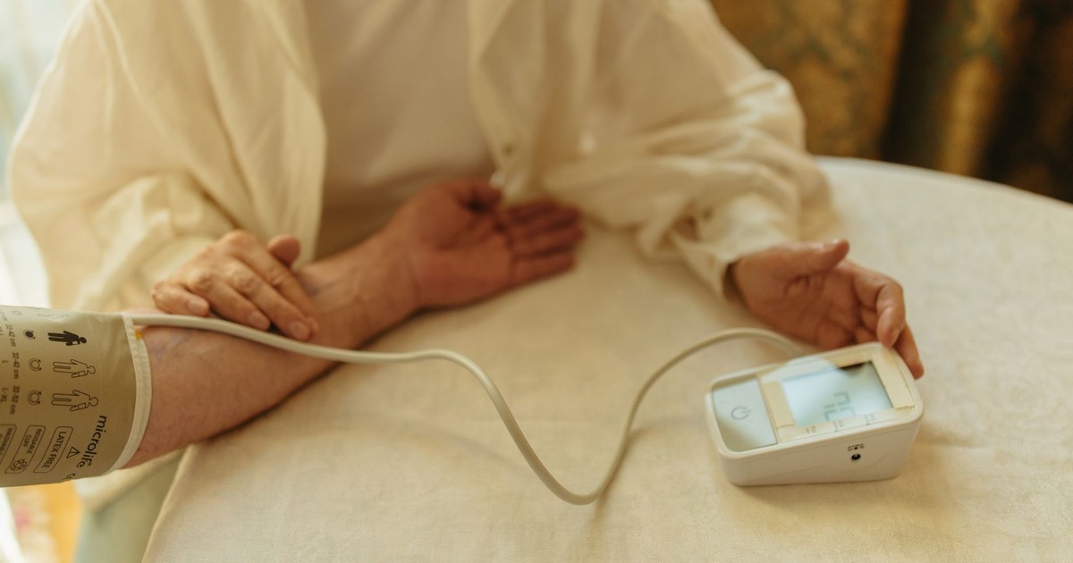 A senior adult checking their blood pressure with a digital monitor at home.