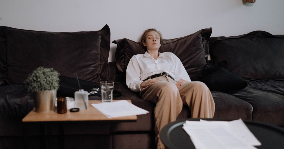 A woman sits tiredly on a couch in a living room, reflecting introspection.