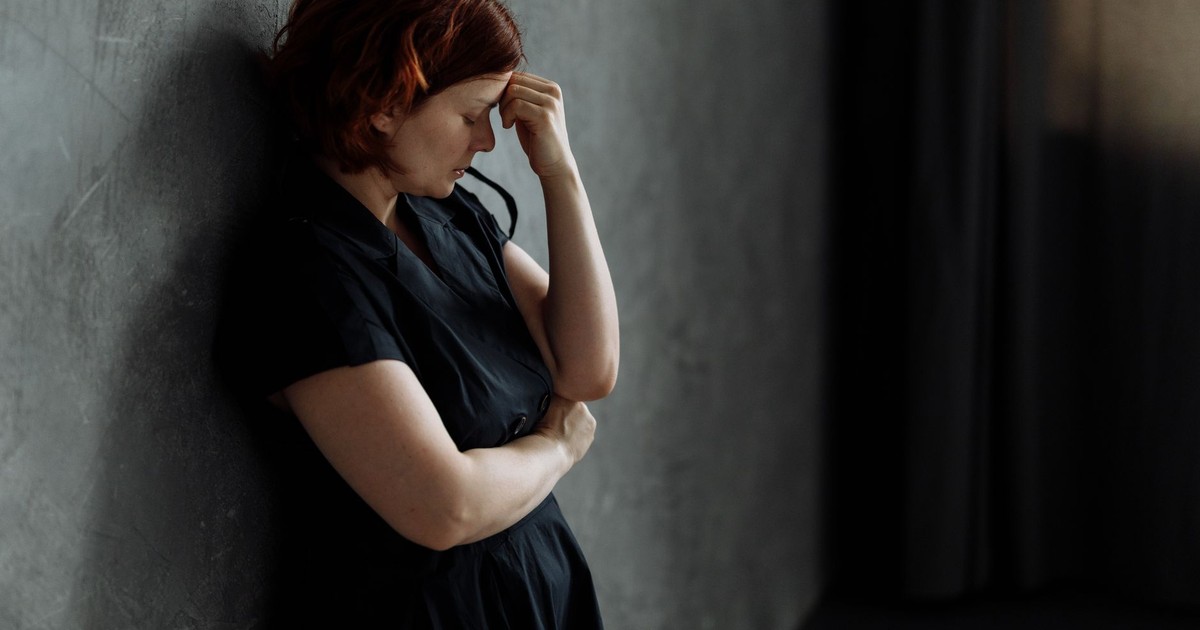 A woman in stress leaning against a concrete wall with eyes closed, conveying deep emotion.