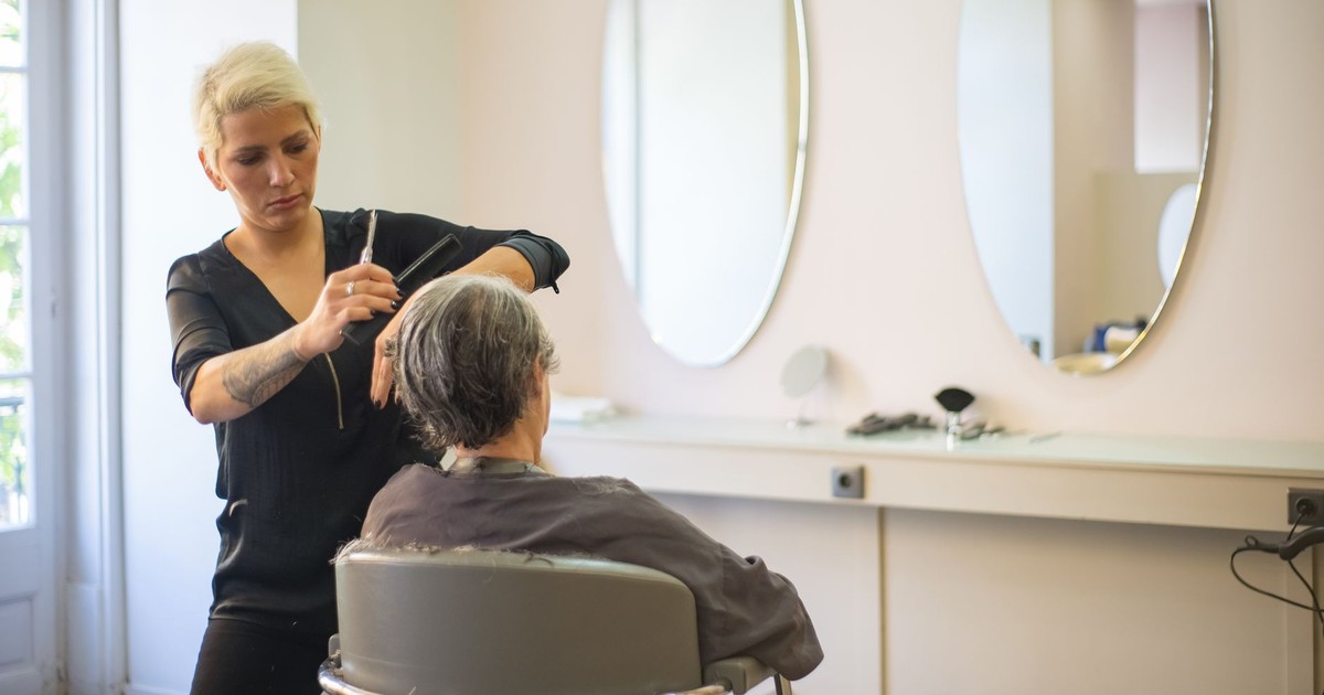 A hairdresser skillfully cuts an elderly woman's hair in a modern salon with mirrors and a comfortable barber chair.
