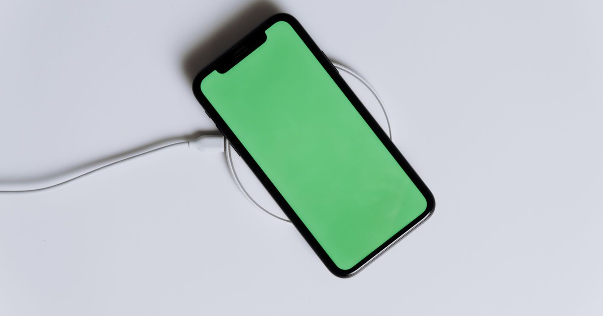 A minimalist smartphone with a green screen on a wireless charger, ideal for tech mockups.
