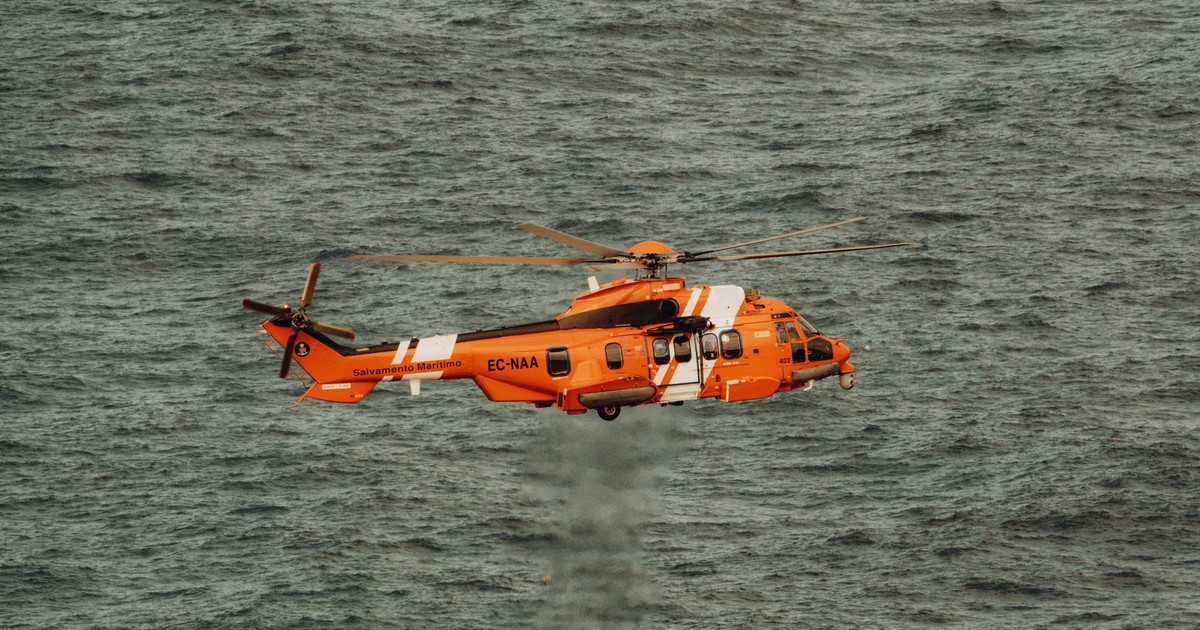An orange rescue helicopter flying over ocean waves, showcasing aerial rescue operations.