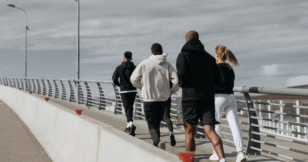 A diverse group of adults jogging together on a city bridge during the day.