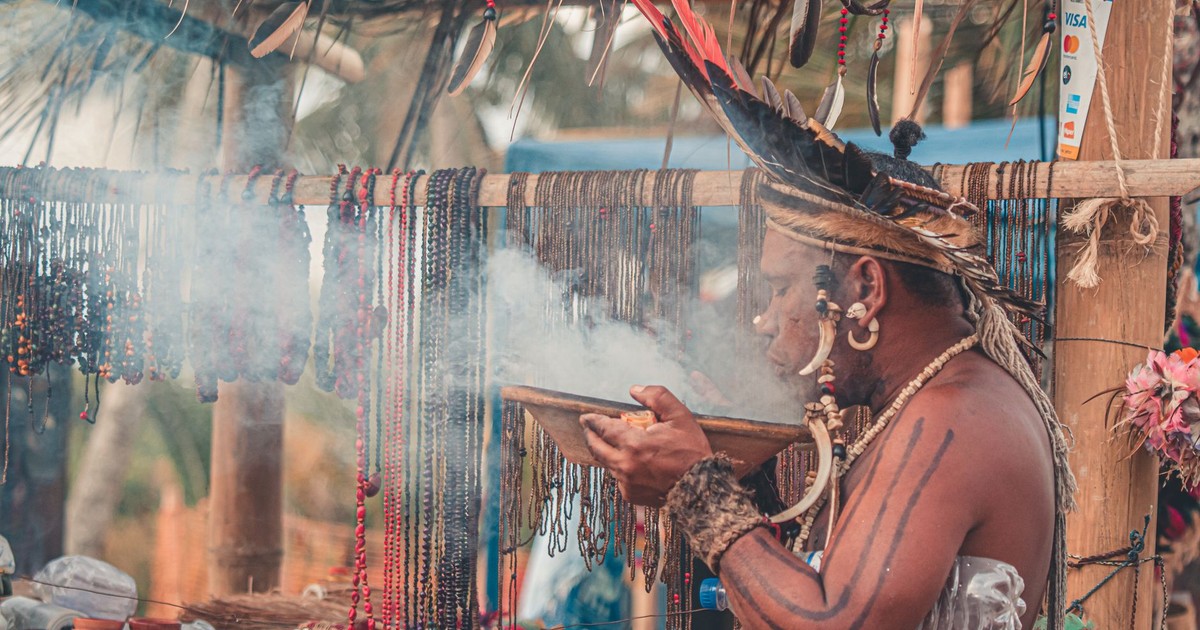 A man in traditional attire participates in an African ceremony, surrounded by smoke and ornaments.