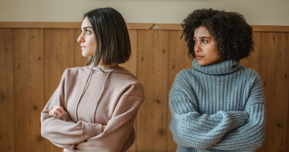 Unhappy African American woman in casual clothes with upset female standing in room with crossed arms while having conflict at home