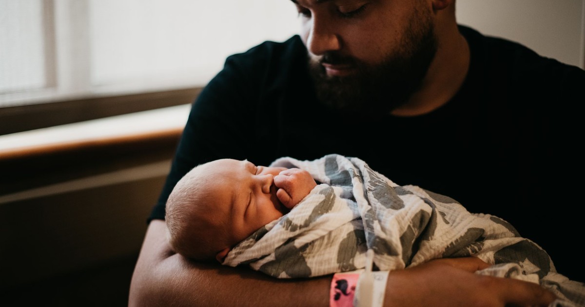 A tender moment of a father holding his newborn baby wrapped in a blanket indoors.