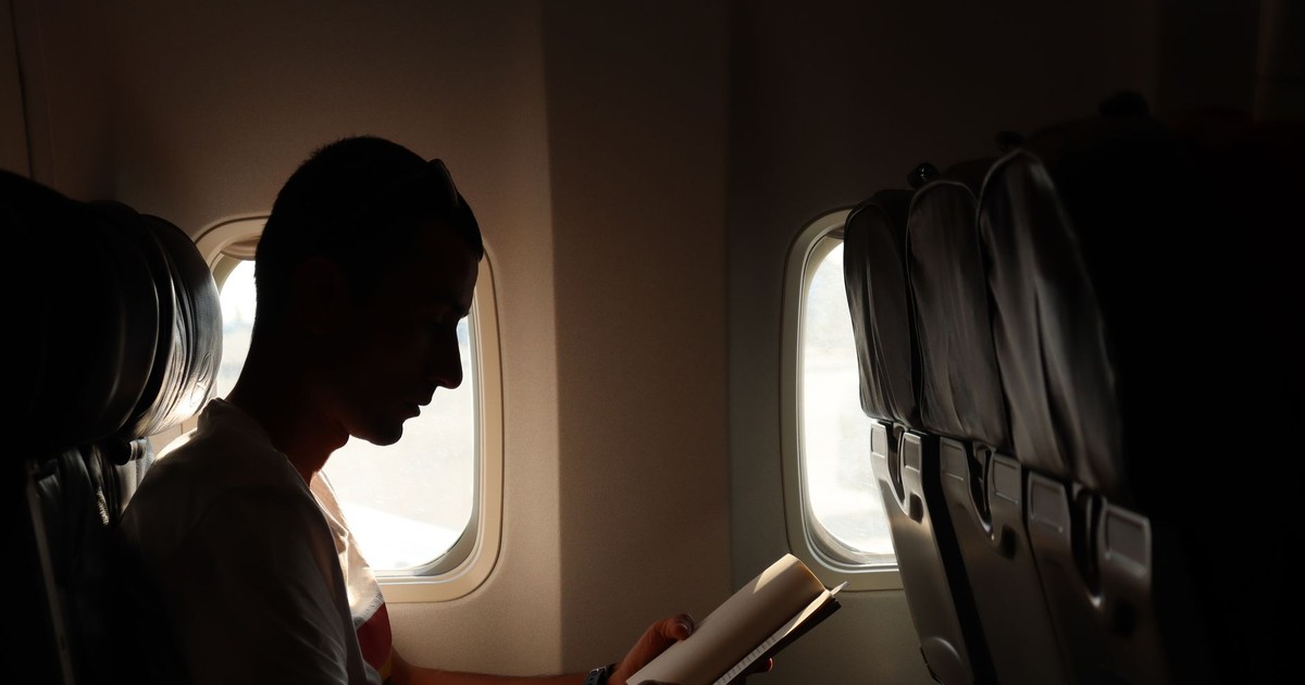 A man reading a book by the window, captured in a silhouette during flight.