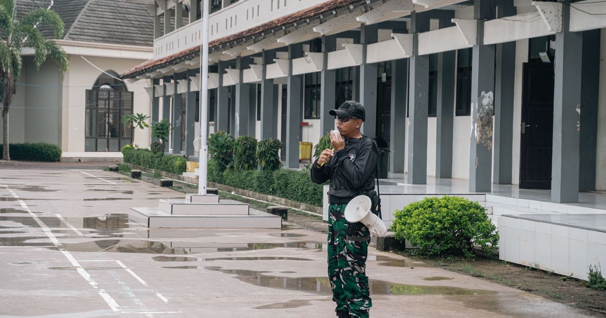 A security guard stands alert with a megaphone outside a building after rain.