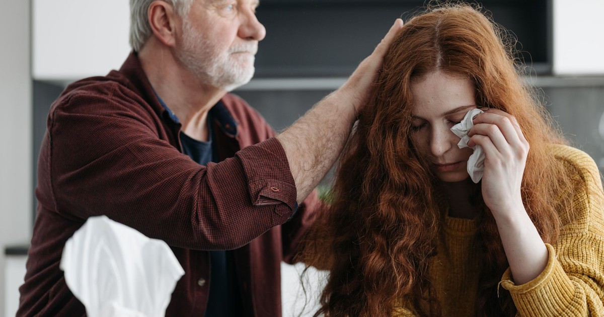 A father consoles his distressed daughter indoors, showcasing love and support.