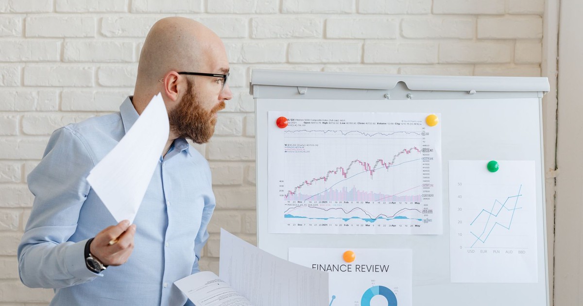 Bald businessman in smart casual attire analyzing financial charts on a whiteboard in an office setting.