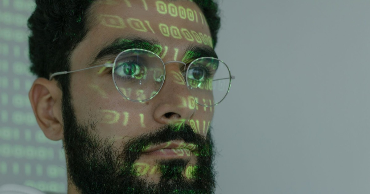A bearded man with digital binary code projected on his face, symbolizing cybersecurity and technology.