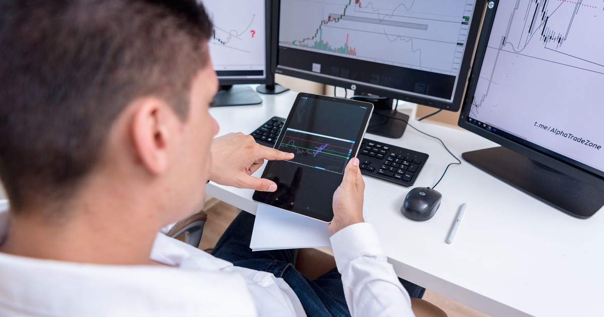 A stock trader analyzing cryptocurrency charts on multiple monitors and a tablet.