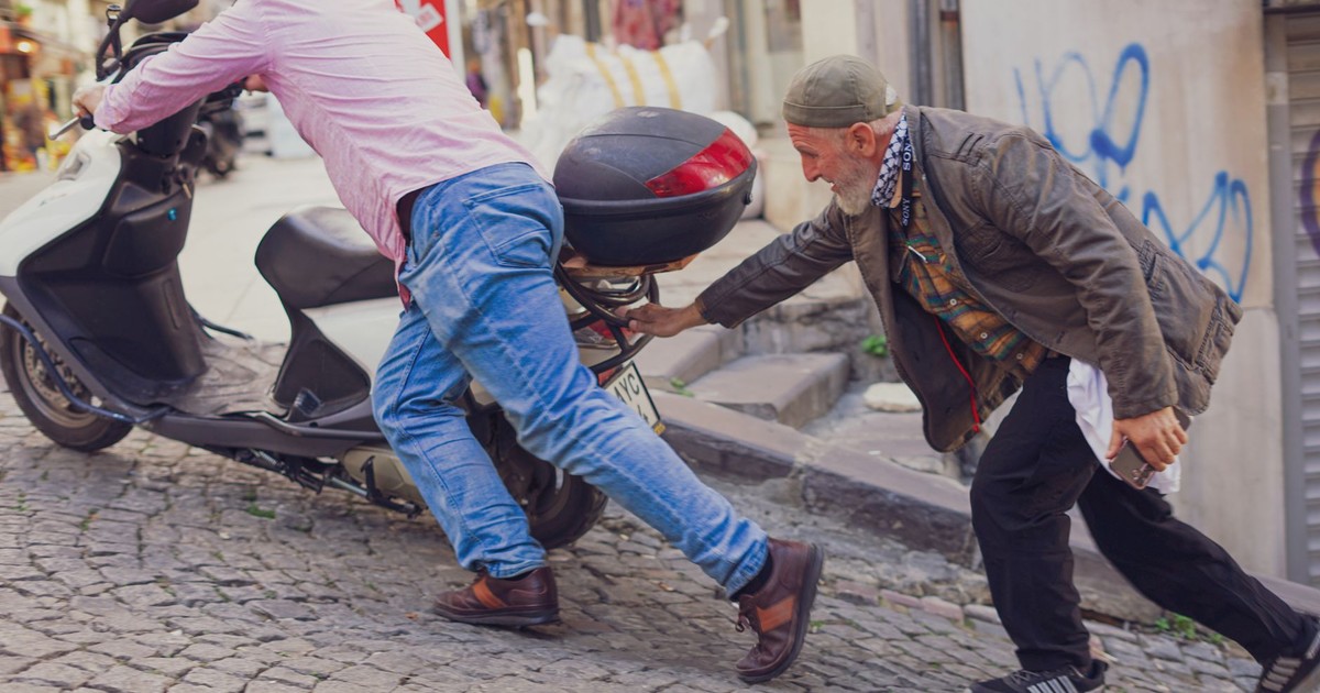 Two men collaborate to push a scooter uphill on a cobblestone street in İstanbul, Türkiye.