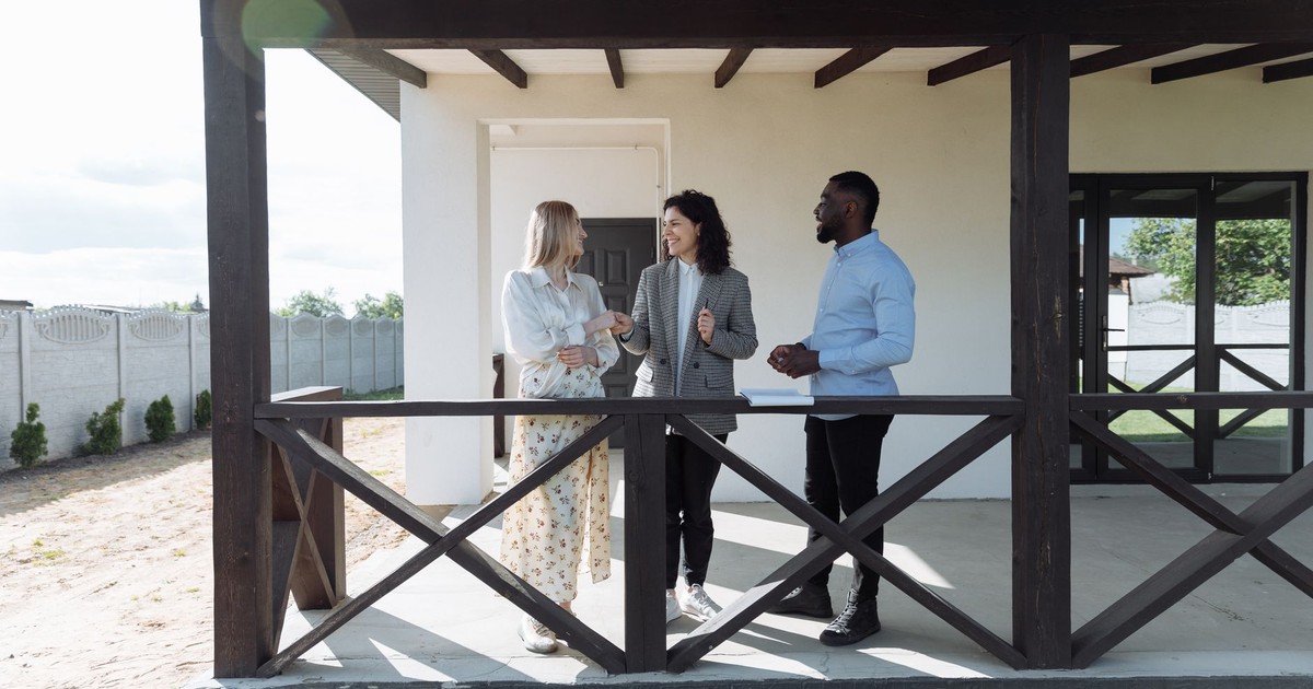 A real estate agent discussing property details with clients on a sunny porch.