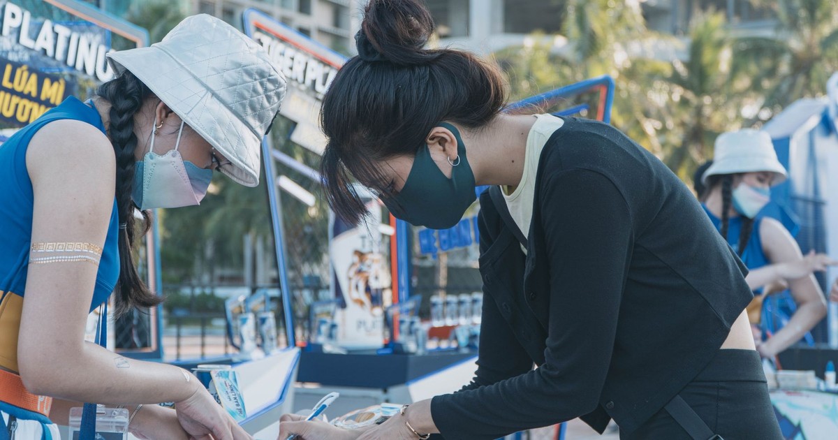 Two young women in masks volunteering outdoors, filling out forms at an event table.