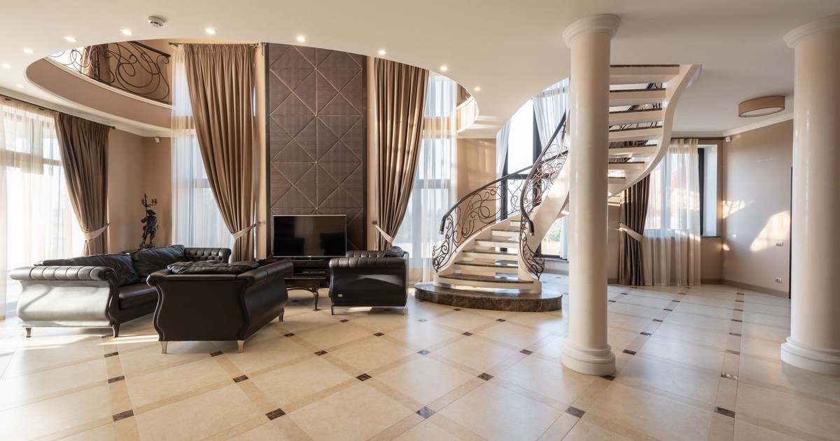 Interior of spacious hallway of classic styled villa with columns and comfortable leather sofa and armchair placed near spiral staircase