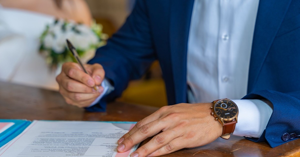 Close-up of groom signing wedding documents with bride nearby.