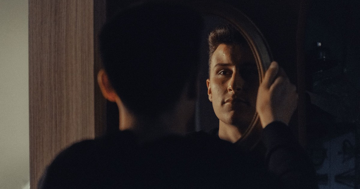A man gazing at his reflection, capturing an introspective moment indoors.