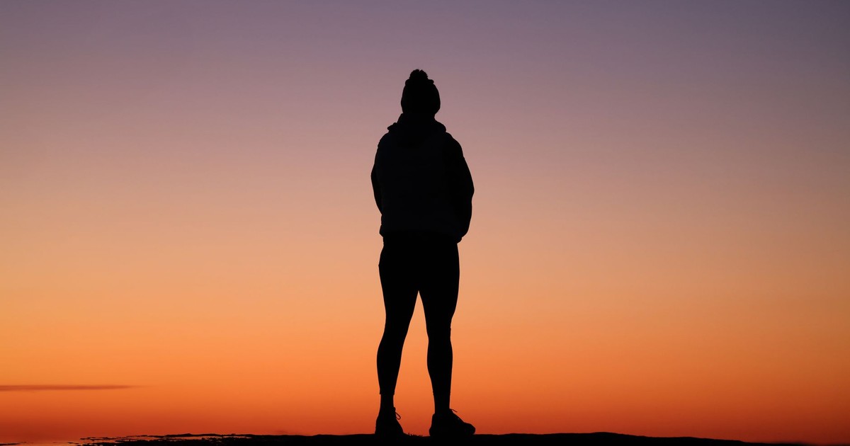 Silhouette of a person standing against a vibrant orange sunset sky, capturing a peaceful evening moment.