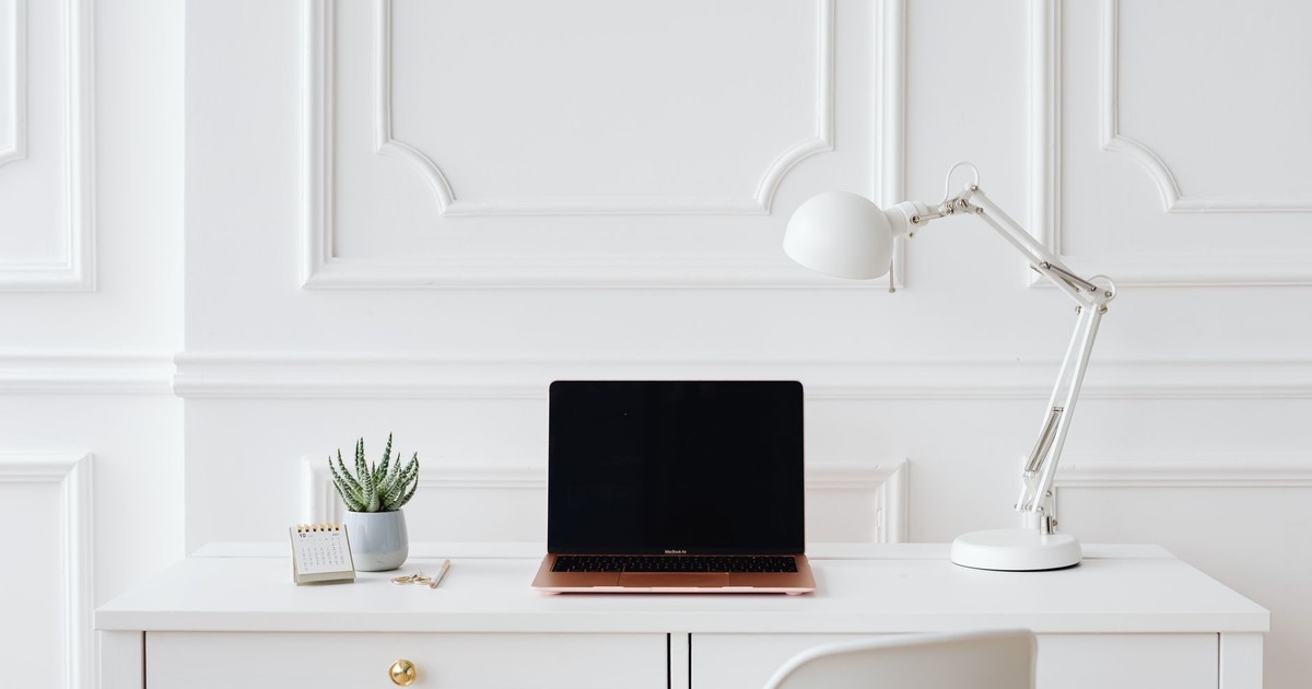 Elegant minimalist desk setup with laptop and white lamp in a bright room.