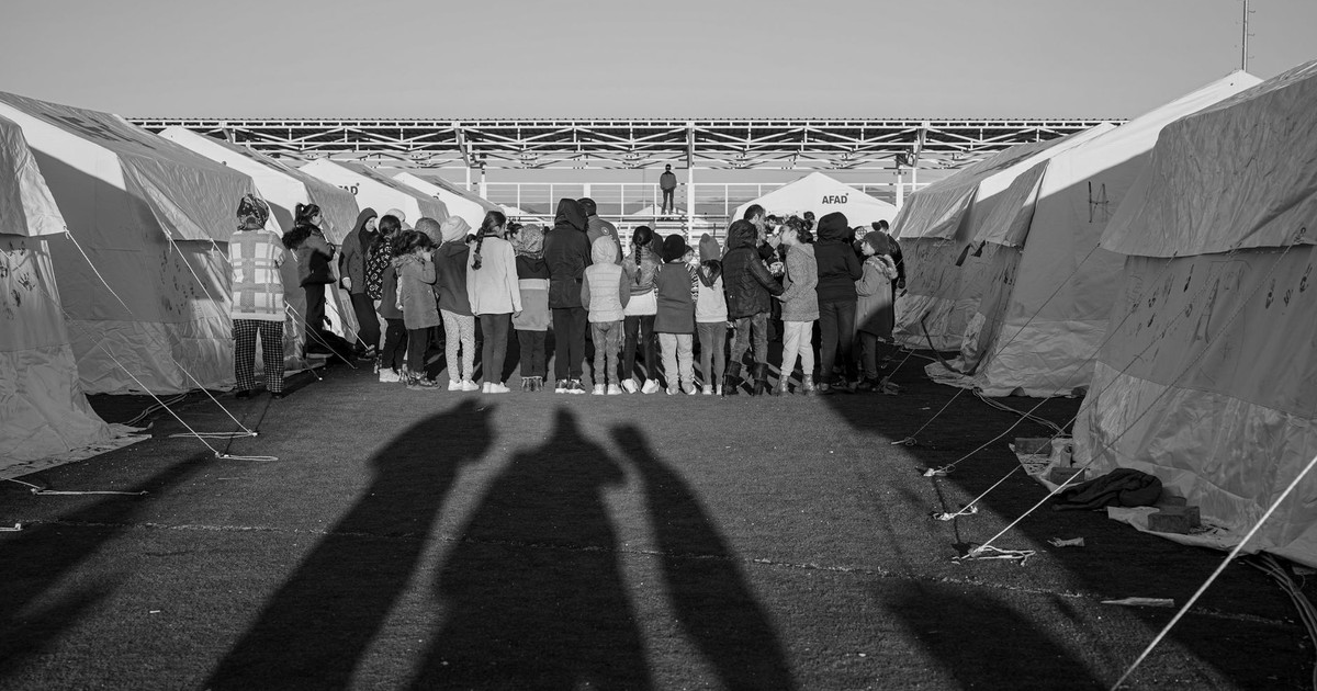 Black and white photo of a group gathered between tents in a Turkish refugee camp.