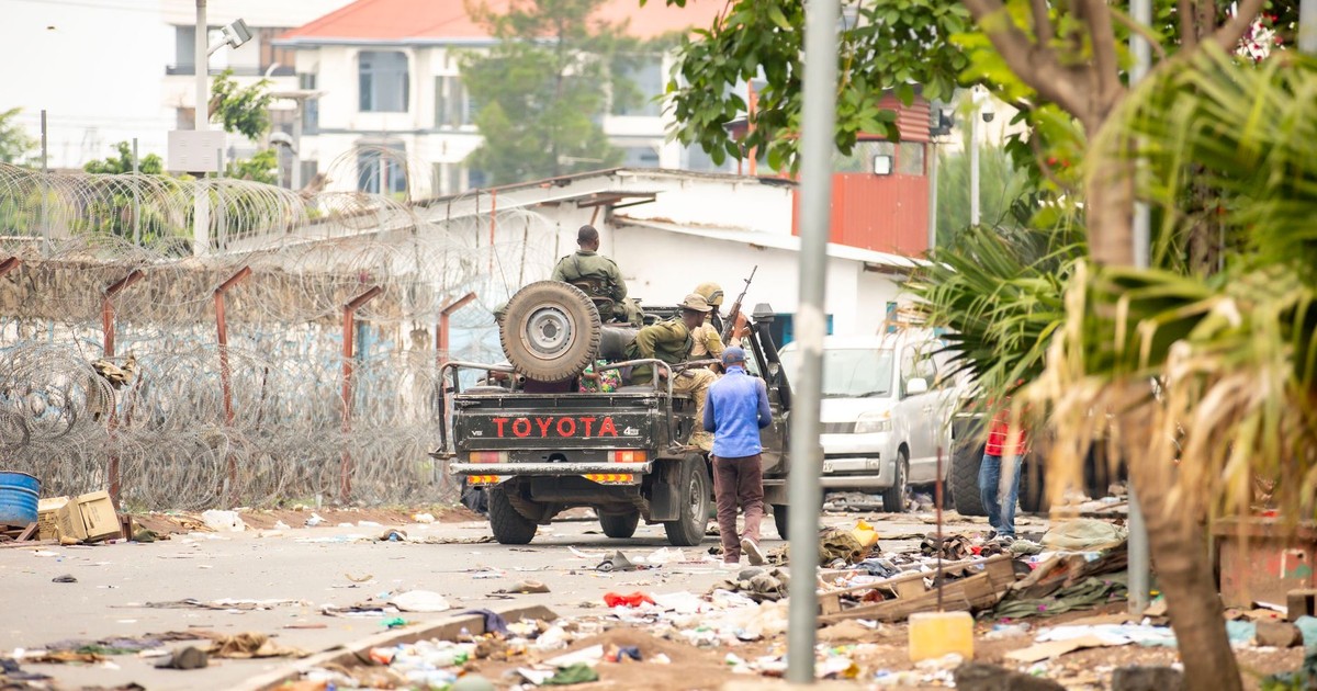 Military personnel patrol a city street with debris in an urban conflict setting.