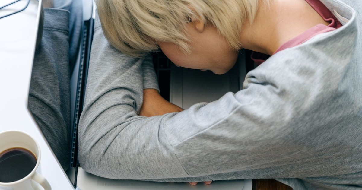 From above of anonymous female in casual clothes resting head on netbook keyboard near cup of coffee after long working day