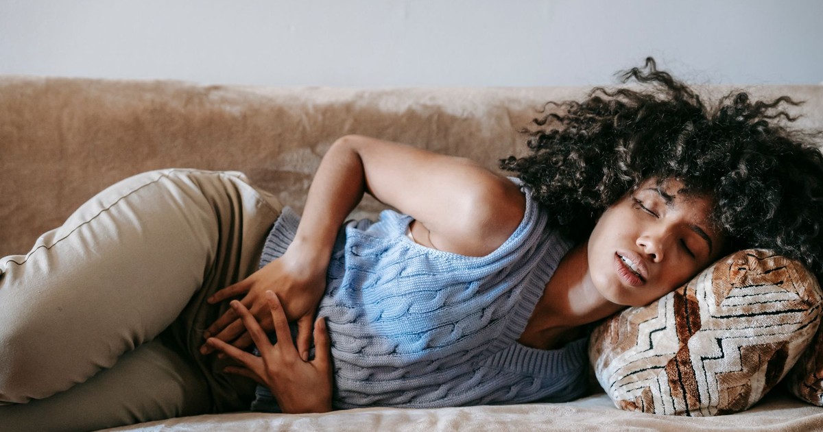 Young African American female with closed eyes lying on sofa while having acute stomach ache