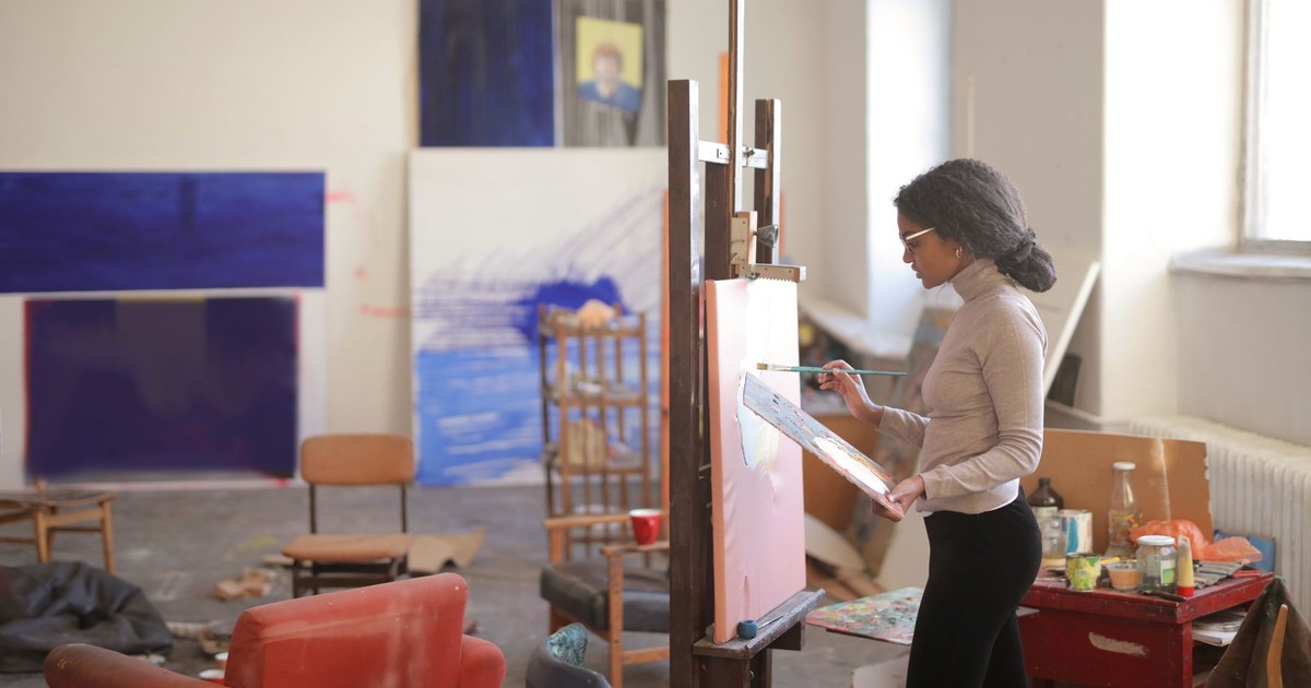 Side view of young black female artist in casual clothes standing near easel and drawing picture while working in studio